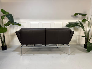 Gebrauchtes braunes Ledersofa Brühl Modell Roro Soft vor einer modernen Wand.