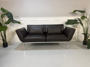 Gebrauchtes braunes Ledersofa Brühl Modell Roro Soft vor einer modernen Wand.