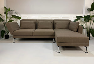 Gebrauchtes braunes Stoff Sofa Brühl Modell Moule vor einer modernen Wand.