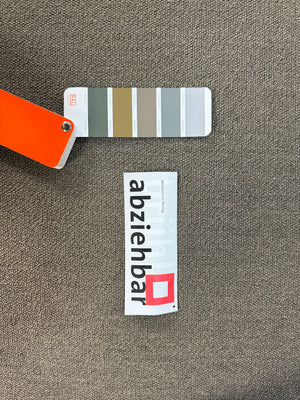 Gebrauchtes braunes Stoff Sofa Brühl Modell Moule vor einer modernen Wand.