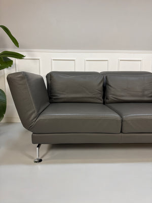Gebrauchtes graues Brühl Moule Designer Leder Sofa vor einer Wand, stilvoll und modern eingerichtet.