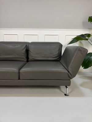 Gebrauchtes graues Brühl Moule Designer Leder Sofa vor einer Wand, stilvoll und modern eingerichtet.