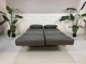 Gebrauchtes graues Brühl Moule Designer Leder Sofa vor einer Wand, stilvoll und modern eingerichtet.