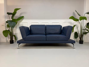 Gebrauchtes Brühl Moule Designer Leder Sofa in der Farbe Blau vor einer Wand, stilvoll und modern eingerichtet.