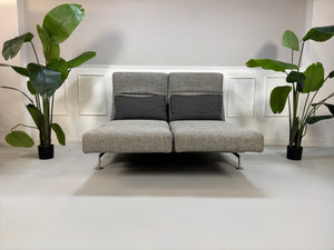 Gebrauchtes Brühl Moule Designer Stoff Sofa in der Farbe Grau vor einer Wand, stilvoll und modern eingerichtet.