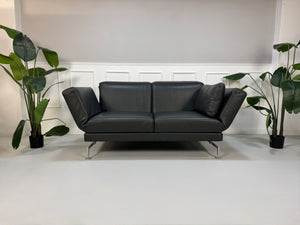 Gebrauchtes Brühl Moule Designer Leder Sofa in der Farbe Grau vor einer Wand, stilvoll und modern eingerichtet.