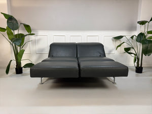 Gebrauchtes Brühl Moule Designer Leder Sofa in der Farbe Grau vor einer Wand, stilvoll und modern eingerichtet.