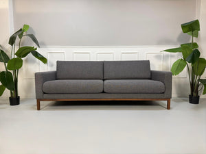 Gebrauchtes graues Bolia North Designer Stoff Sofa vor einer Wand, stilvoll und modern eingerichtet.