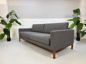 Gebrauchtes graues Bolia North Designer Stoff Sofa vor einer Wand, stilvoll und modern eingerichtet.
