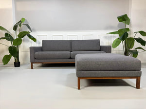 Gebrauchtes graues Bolia North Designer Stoff Sofa vor einer Wand, stilvoll und modern eingerichtet.