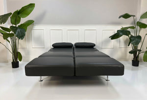 Gebrauchtes graues Brühl Moule Small Designer Leder Sofa vor einer Wand, stilvoll und modern eingerichtet.