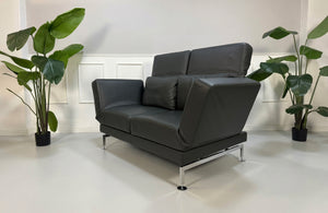 Gebrauchtes graues Brühl Moule Small Designer Leder Sofa vor einer Wand, stilvoll und modern eingerichtet.
