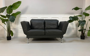 Gebrauchtes graues Brühl Moule Small Designer Leder Sofa vor einer Wand, stilvoll und modern eingerichtet.