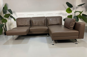 Gebrauchtes braunes Brühl Moule Designer Leder Sofa vor einer Wand, stilvoll und modern eingerichtet.