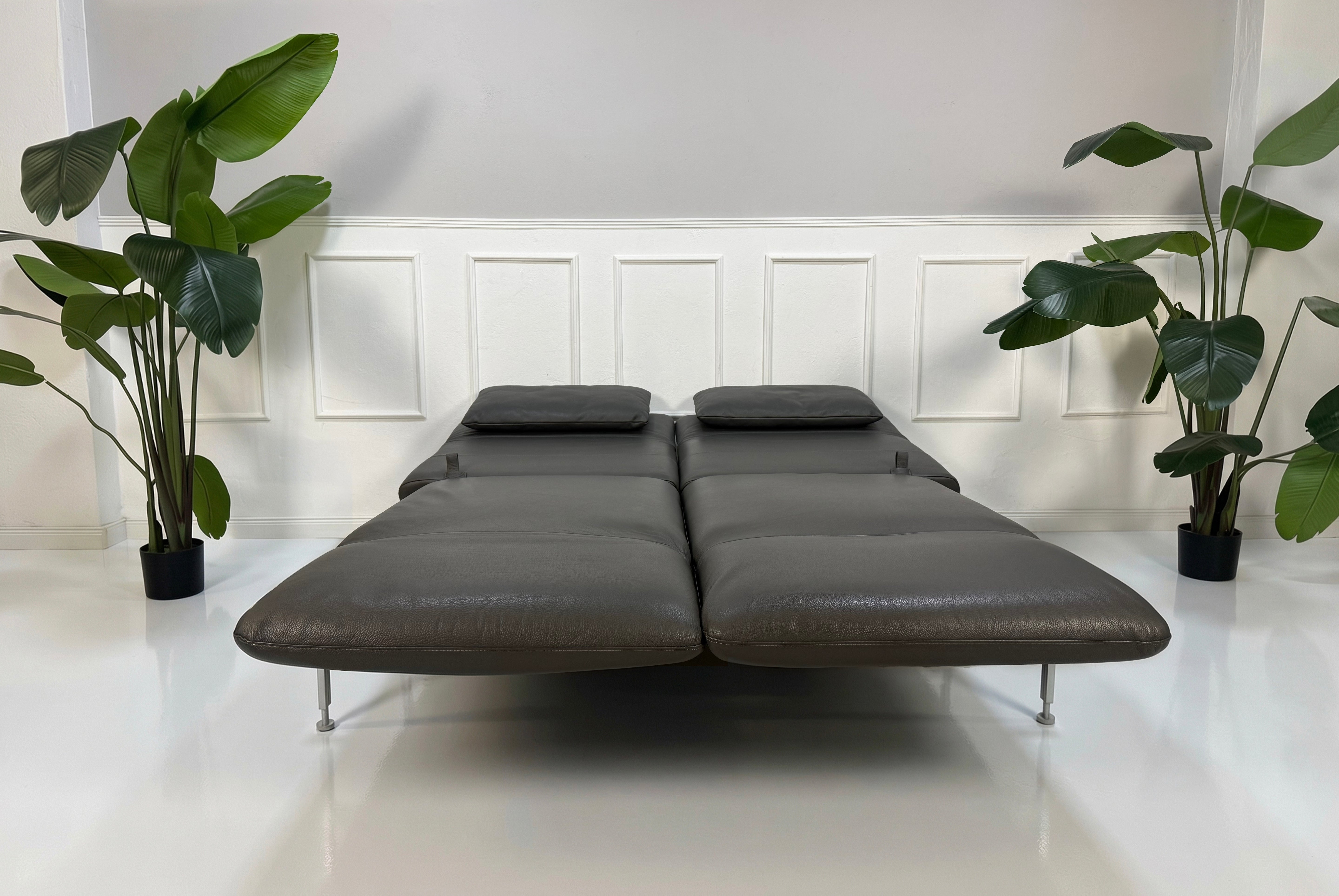 Gebrauchtes graues Brühl Roro Medium Designer Leder Sofa vor einer Wand, stilvoll und modern eingerichtet.