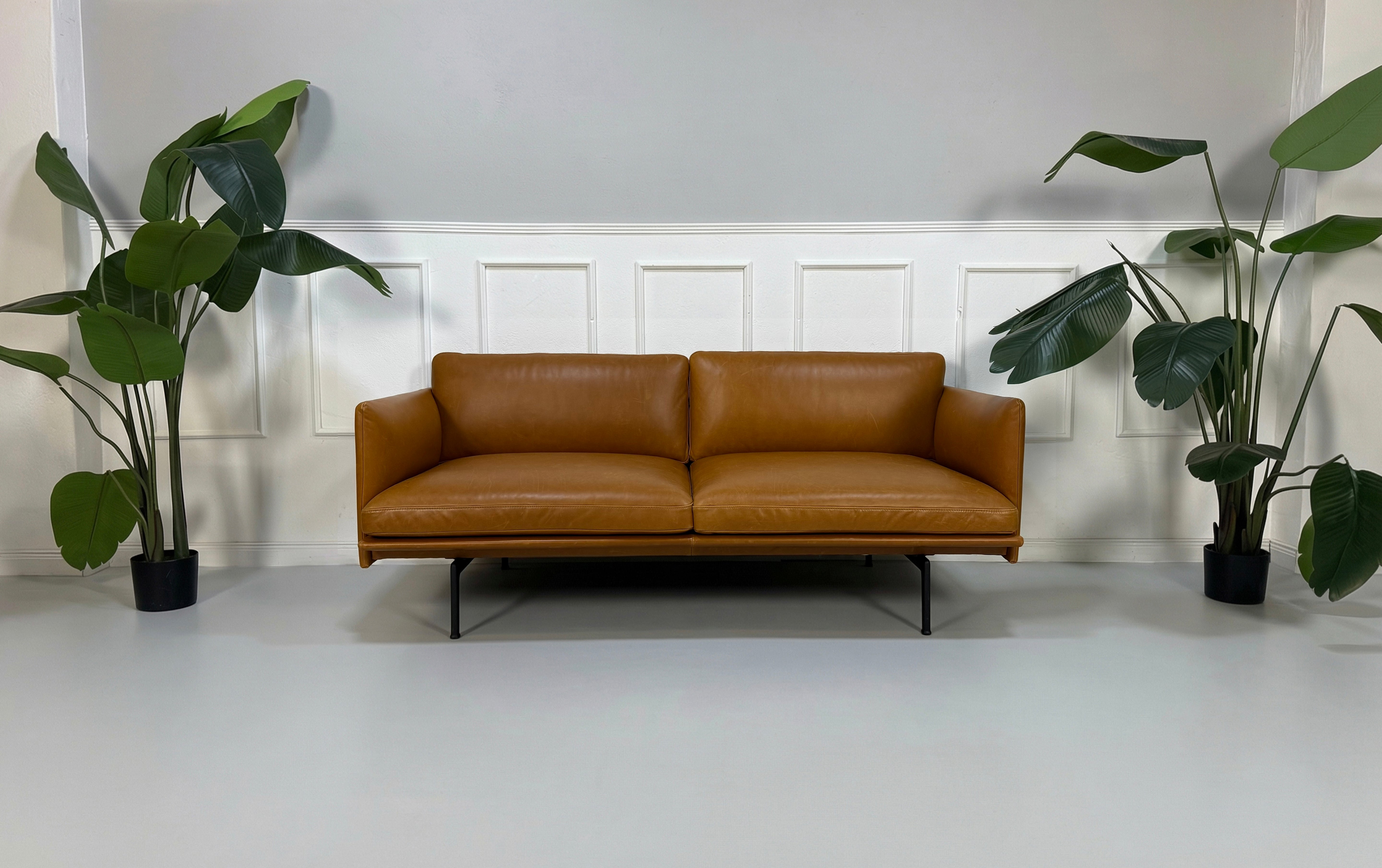 Gebrauchtes braunes cognac Muuto Outline Designer Leder Sofa vor einer Wand, stilvoll und modern eingerichtet.