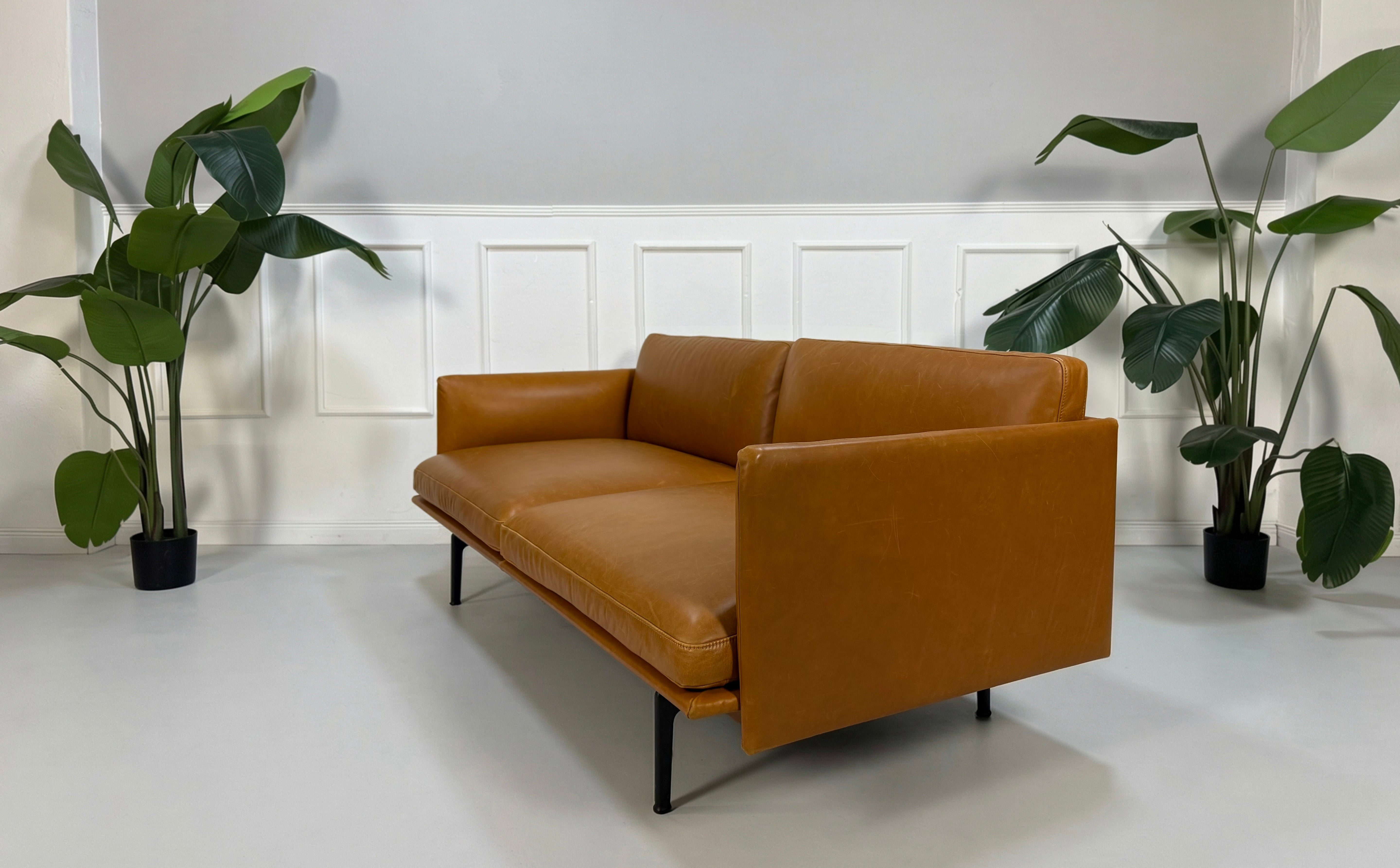 Gebrauchtes braunes cognac Muuto Outline Designer Leder Sofa vor einer Wand, stilvoll und modern eingerichtet.