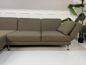 Gebrauchtes braunes Brühl Moule Designer Stoff Sofa vor einer Wand, stilvoll und modern eingerichtet.