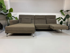 Gebrauchtes braunes Brühl Moule Designer Stoff Sofa vor einer Wand, stilvoll und modern eingerichtet.