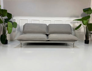 Gebrauchtes graues Rolf Benz Nova Designer Stoff Sofa vor einer Wand, stilvoll und modern eingerichtet.
