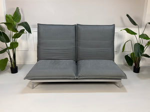 Gebrauchtes graues Rolf Benz Nova Designer Stoff Sofa vor einer Wand, stilvoll und modern eingerichtet.