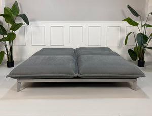 Gebrauchtes graues Rolf Benz Nova Designer Stoff Sofa vor einer Wand, stilvoll und modern eingerichtet.