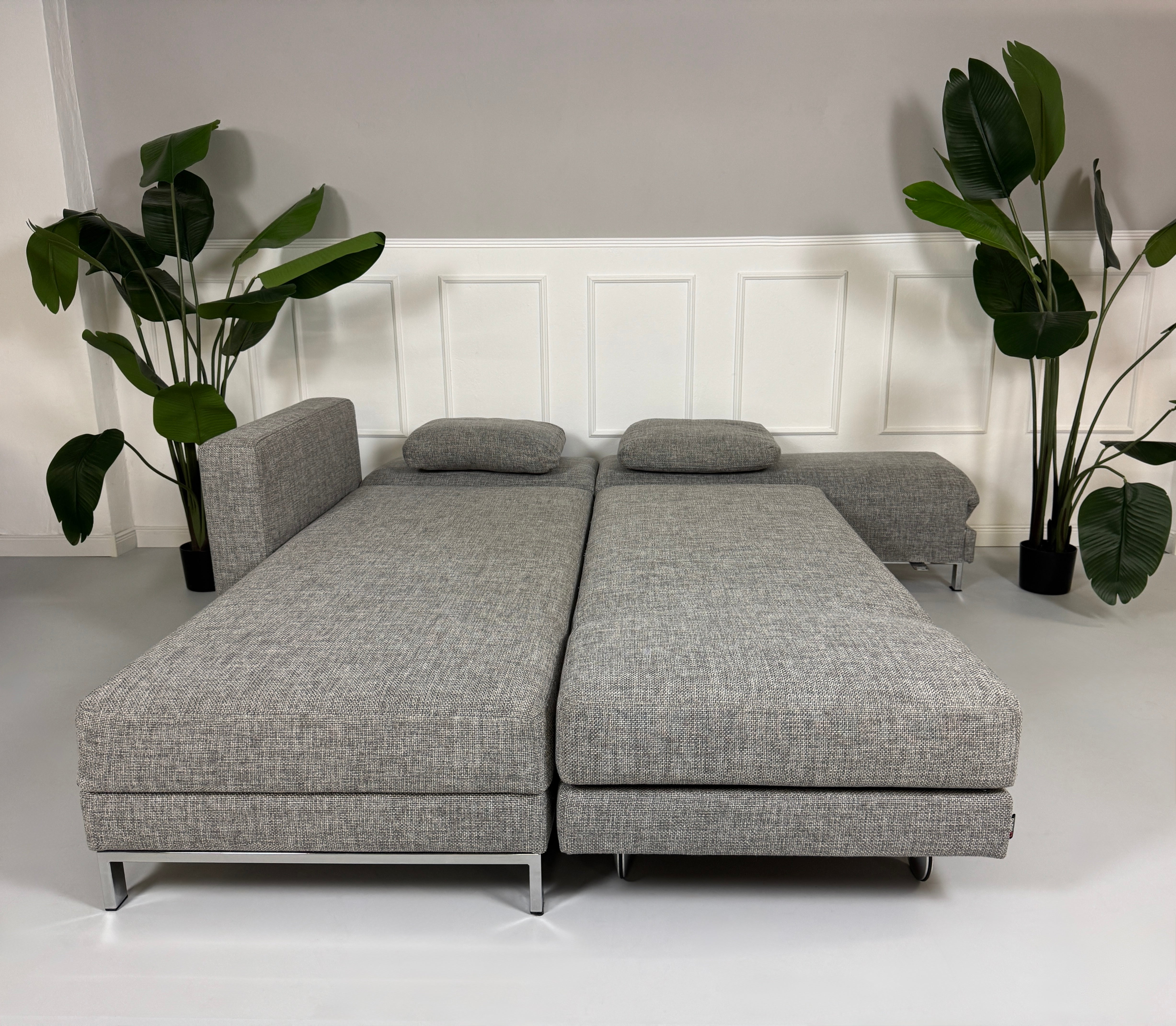 Gebrauchtes graues Brühl Four Two Designer Stoff Sofa vor einer Wand, stilvoll und modern eingerichtet.