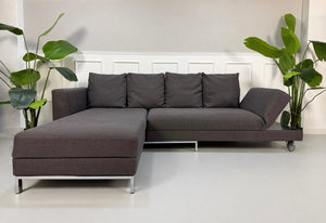 Gebrauchtes grau blaues Brühl Four Two Designer Stoff Sofa vor einer Wand, stilvoll und modern eingerichtet.