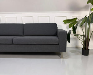 Gebrauchtes graues Bolia Scandinavia Designer Stoff Sofa vor einer Wand, stilvoll und modern eingerichtet.