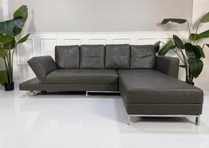 Gebrauchtes graues Brühl Fourwto Designer Leder Sofa vor einer Wand, stilvoll und modern eingerichtet.