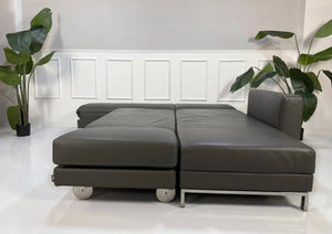Gebrauchtes graues Brühl Fourwto Designer Leder Sofa vor einer Wand, stilvoll und modern eingerichtet.