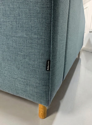 Gebrauchtes blaues Bolia Scandinavia Designer Stoff Sofa vor einer Wand, stilvoll und modern eingerichtet.