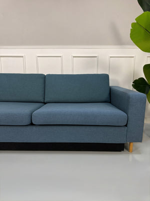 Gebrauchtes blaues Bolia Scandinavia Designer Stoff Sofa vor einer Wand, stilvoll und modern eingerichtet.