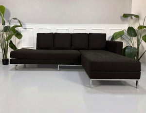 Gebrauchtes braunes Brühl Fourtwo Designer Stoff Sofa mit Hocker vor einer Wand, stilvoll und modern eingerichtet.