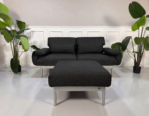 Gebrauchtes graues Rolf Benz Plura Designer Stoff Sofa mit Hocker vor einer Wand, stilvoll und modern eingerichtet.