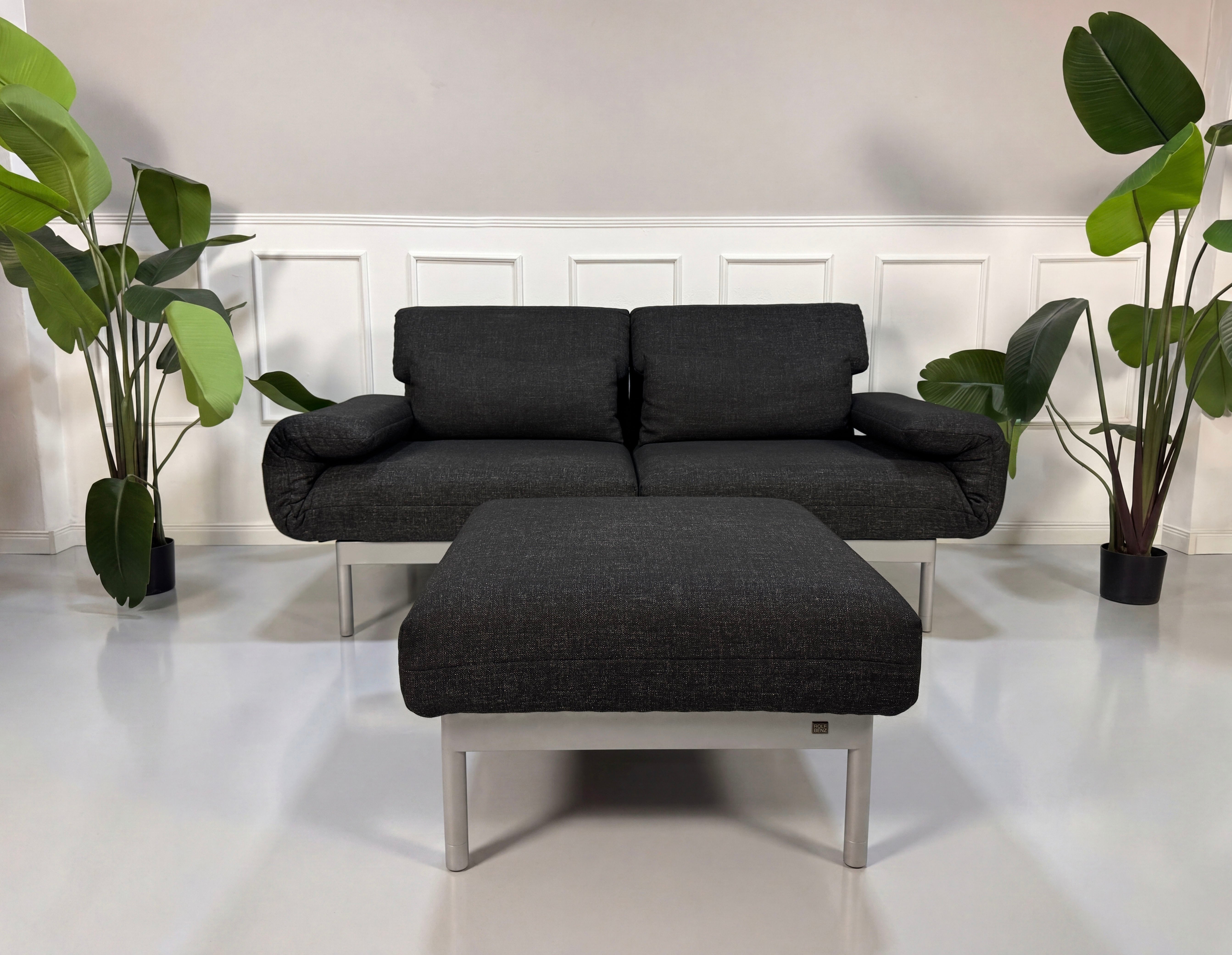 Gebrauchtes graues Rolf Benz Plura Designer Stoff Sofa mit Hocker vor einer Wand, stilvoll und modern eingerichtet.