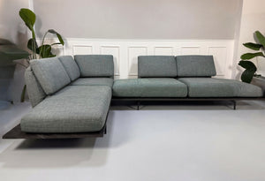 Gebrauchtes blau graues Rolf Benz Aura Designer Stoff Sofa vor einer Wand, stilvoll und modern eingerichtet.