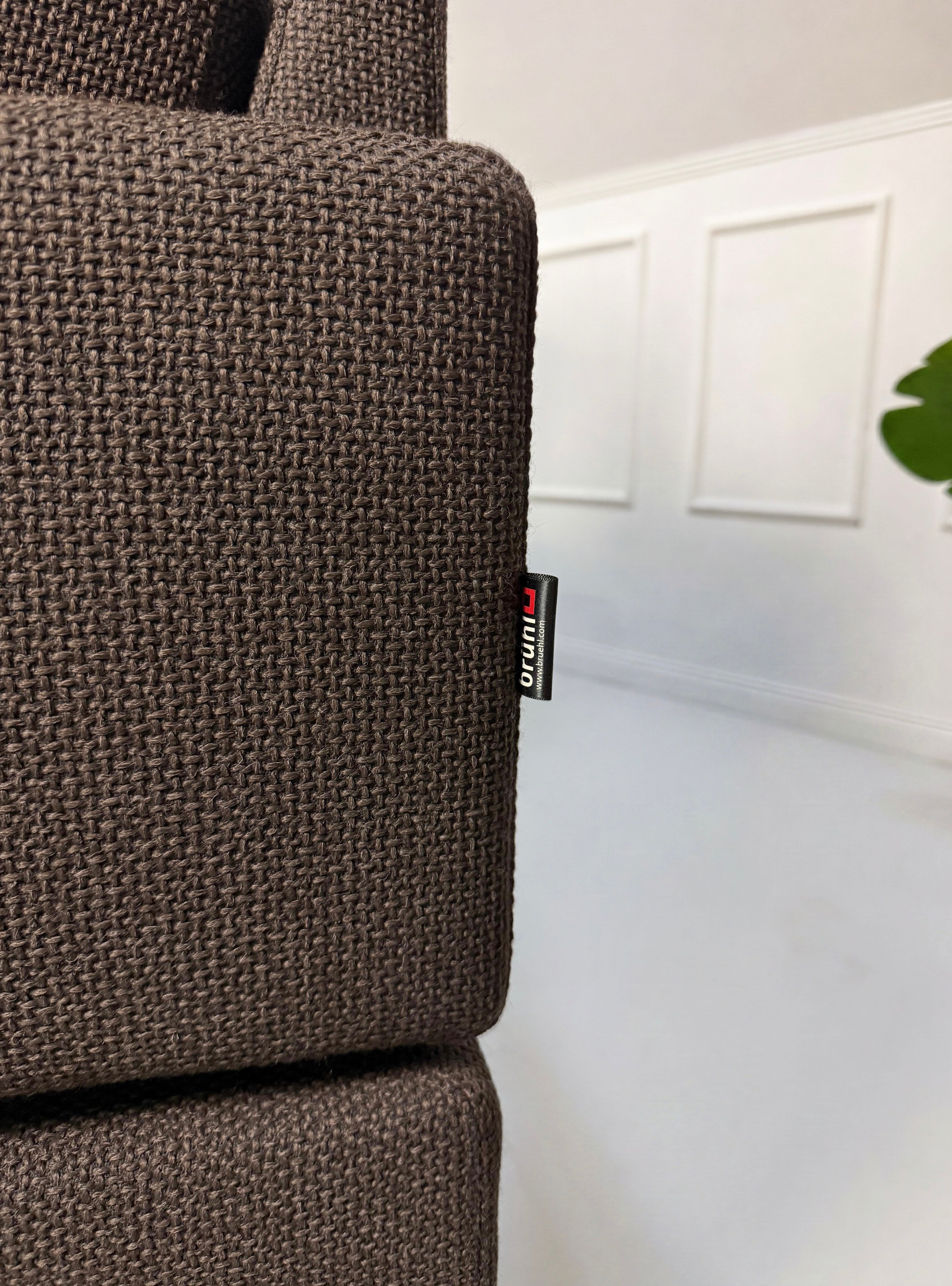 Gebrauchtes braunes Brühl Ecksofa Designer Stoff Sofa vor einer Wand, stilvoll und modern eingerichtet.