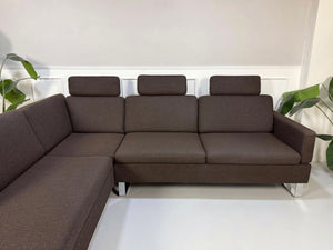 Gebrauchtes braunes Brühl Ecksofa Designer Stoff Sofa vor einer Wand, stilvoll und modern eingerichtet.