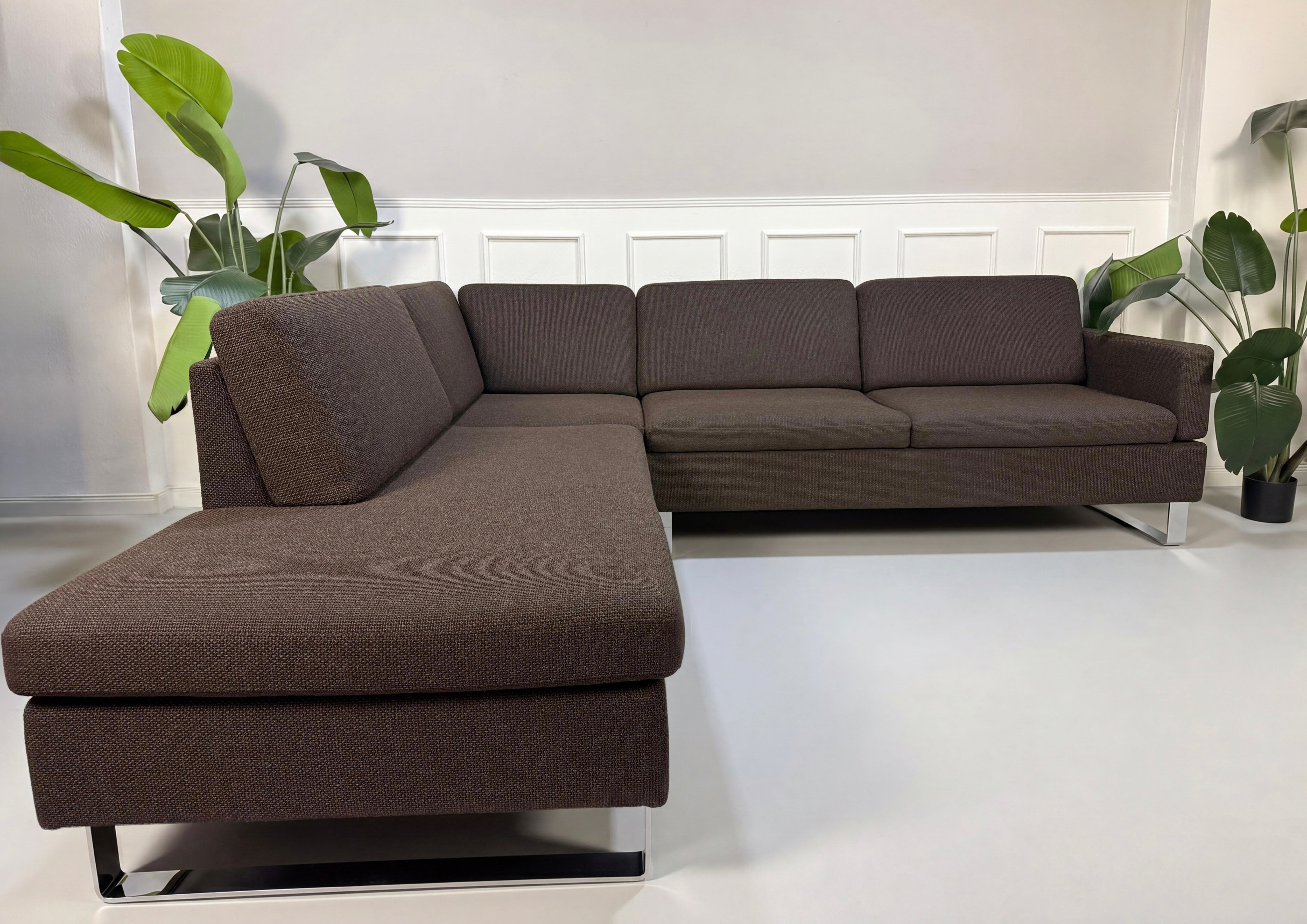 Gebrauchtes braunes Brühl Ecksofa Designer Stoff Sofa vor einer Wand, stilvoll und modern eingerichtet.