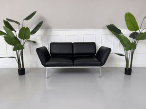 Gebrauchtes schwarzes Brühl Roro Small Designer Leder Sofa vor einer Wand, stilvoll und modern eingerichtet.