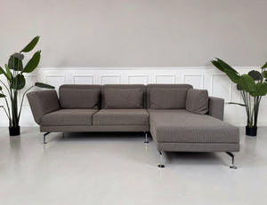Gebrauchtes braun graues Brühl Moule Designer Stoff Sofa vor einer Wand, stilvoll und modern eingerichtet.