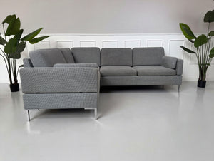 Gebrauchtes graues Brühl Alba Designer Stoff Sofa vor einer Wand, stilvoll und modern eingerichtet.