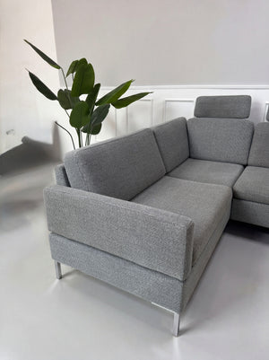 Gebrauchtes graues Brühl Alba Designer Stoff Sofa vor einer Wand, stilvoll und modern eingerichtet.