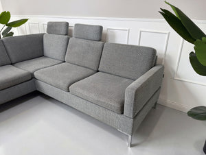Gebrauchtes graues Brühl Alba Designer Stoff Sofa vor einer Wand, stilvoll und modern eingerichtet.