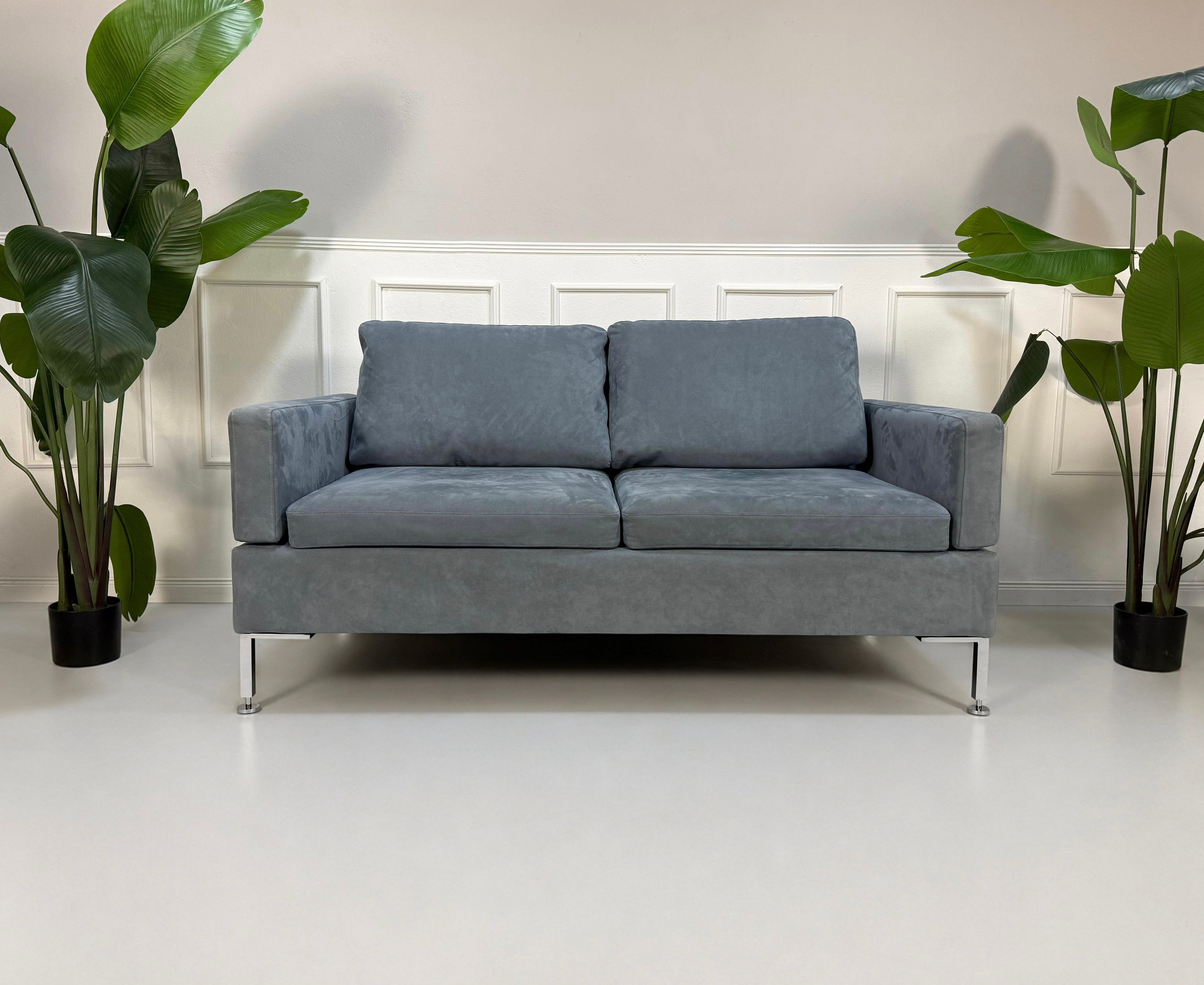 Gebrauchtes blaues Brühl Alba Designer Stoff Sofa vor einer Wand, stilvoll und modern eingerichtet.
