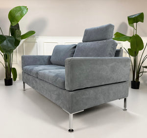 Gebrauchtes blaues Brühl Alba Designer Stoff Sofa vor einer Wand, stilvoll und modern eingerichtet.
