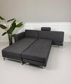 Gebrauchtes graues Brühl Four Two Designer Stoff Sofa vor einer Wand, stilvoll und modern eingerichtet.
