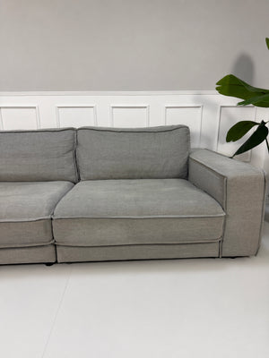 Gebrauchtes graues Bolia Noora Designer Stoff Sofa vor einer Wand, stilvoll und modern eingerichtet.