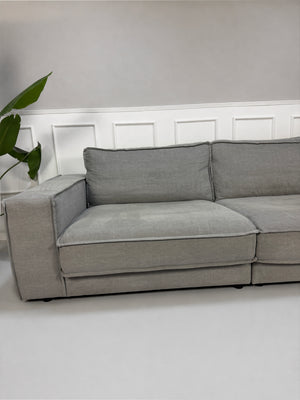 Gebrauchtes graues Bolia Noora Designer Stoff Sofa vor einer Wand, stilvoll und modern eingerichtet.
